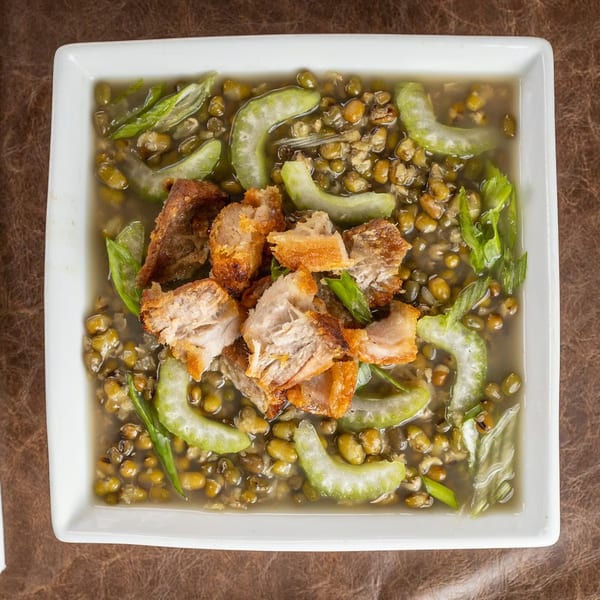 Mung bean stew with crispy pork belly and bitter melon in a white square bowl.