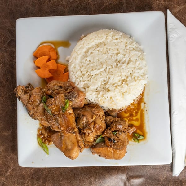 Chicken adobo with white rice and sliced carrots on a white rectangular plate.